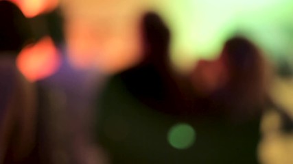 Blurred silhouettes of dancing people out of focus at a concert or disco, on the dance floor in a nightclub at a party under colorful spotlights. Out of focus