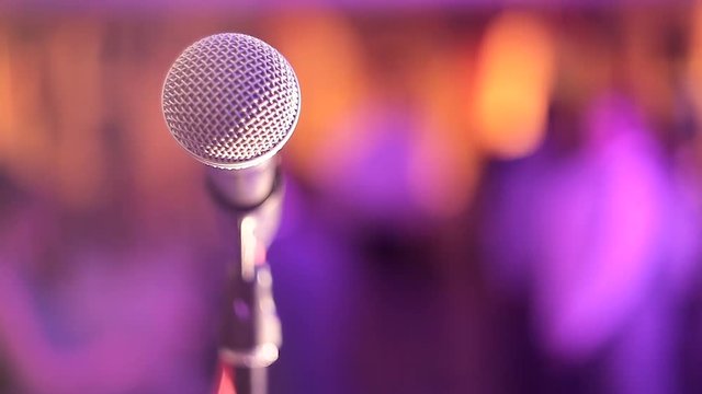 The microphone on the stand is on the stage, the microphone is close up against the background of the hall. Point of view of the singer. Microphone on an abstract blurred color background.