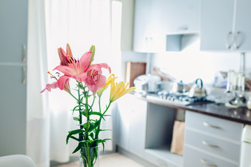 Colorful lilies. Modern kitchen design. Interior of white and silver kitchen decorated with flowers.