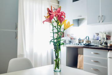 Colorful lilies. Modern kitchen design. Interior of white and silver kitchen decorated with flowers.