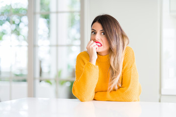 Young beautiful woman wearing winter sweater at home looking stressed and nervous with hands on mouth biting nails. Anxiety problem.