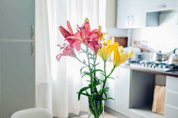 Colorful lilies. Modern kitchen design. Interior of white and silver kitchen decorated with flowers.