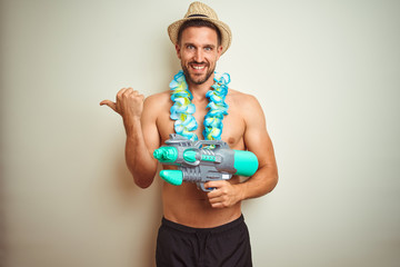 Handsome shirtless man wearing hawaiian lei and water gun over background pointing and showing with...