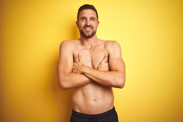 Fototapeta premium Young handsome shirtless man over isolated yellow background happy face smiling with crossed arms looking at the camera. Positive person.