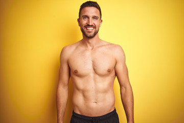Young handsome shirtless man over isolated yellow background with a happy and cool smile on face....