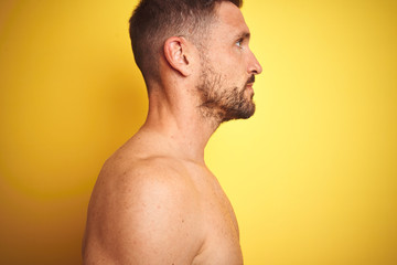 Naklejka premium Sexy young shirtless man showing nude fitness chest over yellow isolated background looking to side, relax profile pose with natural face with confident smile.