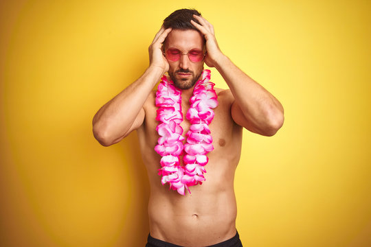 Young handsome shirtless man wearing sunglasses and pink hawaiian lei over yellow background suffering from headache desperate and stressed because pain and migraine. Hands on head.