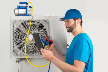 Installation service repair of an air conditioner outdoor unit, by cryogenist technican worker evacuate the system with vacuum pump and manifold gauges tablet in blue shirt baseball cap - obrazy, fototapety, plakaty
