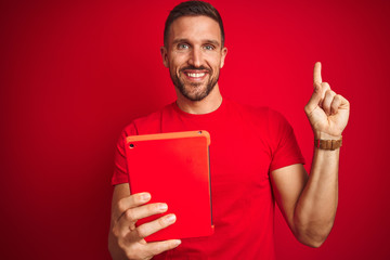 Young man using digital touchpad tablet over red isolated background very happy pointing with hand and finger to the side