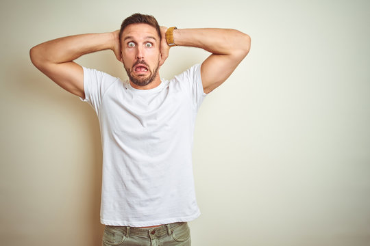 Young handsome man wearing casual white t-shirt over isolated background Crazy and scared with hands on head, afraid and surprised of shock with open mouth