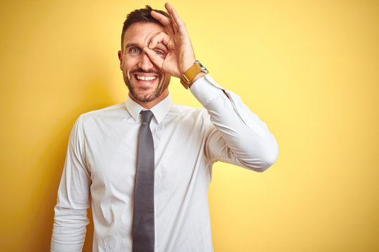 Young handsome business man wearing elegant white shirt over yellow isolated background doing ok gesture with hand smiling, eye looking through fingers with happy face.