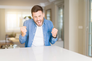 Young handsome man at home very happy and excited doing winner gesture with arms raised, smiling and screaming for success. Celebration concept.