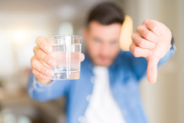 Young handsome man drinking a glass of water at home with angry face, negative sign showing dislike...