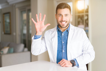 Young handsome doctor man at the clinic showing and pointing up with fingers number five while smiling confident and happy.