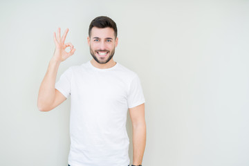 Fototapeta premium Young handsome man wearing casual white t-shirt over isolated background smiling positive doing ok sign with hand and fingers. Successful expression.