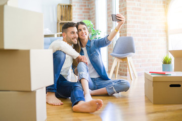 Fototapeta na wymiar Young couple sitting on the floor of new house taking a selfie photo using smartphone, smiling happy for moving to new apartment