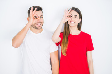Fototapeta na wymiar Young beautiful couple together over white isolated background doing ok gesture with hand smiling, eye looking through fingers with happy face.