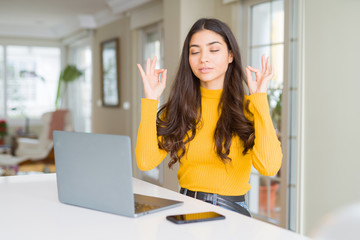 Young woman using computer laptop relax and smiling with eyes closed doing meditation gesture with fingers. Yoga concept.