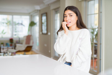Young beautiful woman at home on white table looking stressed and nervous with hands on mouth biting nails. Anxiety problem.