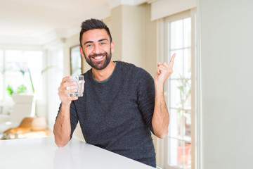 Handsome hispanic man drinking a fresh glass of water very happy pointing with hand and finger to the side