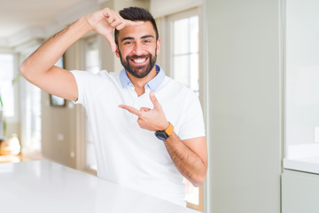 Handsome hispanic man casual white t-shirt at home smiling making frame with hands and fingers with happy face. Creativity and photography concept.