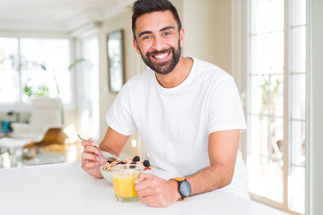 Handsome man smiling eating healthy breakfast and drinking orange juice in the morning