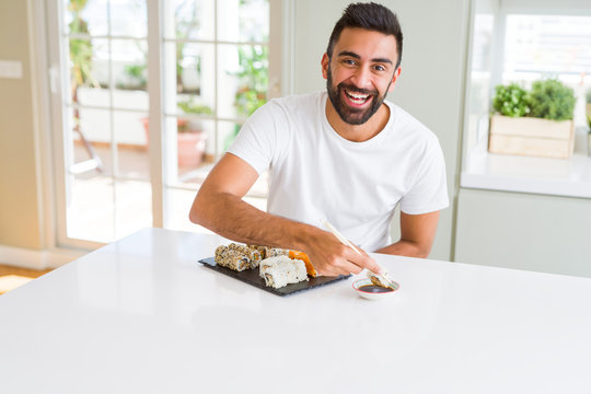 Handsome man smiling happy enjoying eating fresh colorful asian sushi using chopsticks