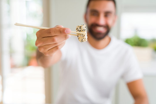 Handsome man smiling happy enjoying eating fresh colorful asian sushi using chopsticks