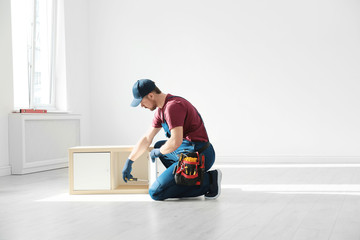 Handyman in uniform assembling furniture indoors, space for text. Professional construction tools