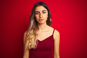 Naklejka premium Young beautiful woman wearing a t-shirt over red isolated background with serious expression on face. Simple and natural looking at the camera.