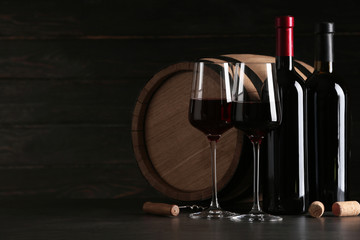Composition with glasses and bottles of red wine on table against dark background. Space for text