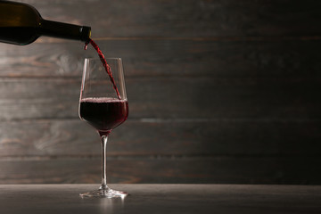 Pouring red wine into glass from bottle on table against wooden background. Space for text