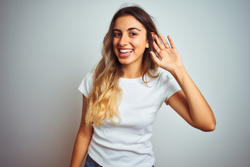 Young beautiful woman wearing casual white t-shirt over isolated background smiling with hand over ear listening an hearing to rumor or gossip. Deafness concept.