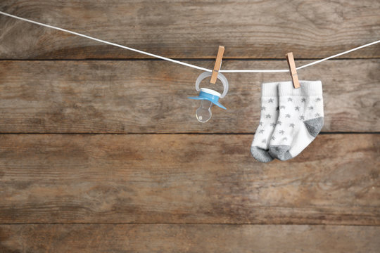 Pair of socks and pacifier on laundry line against wooden background, space for text. Baby accessories