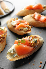 Tasty bruschettas with salmon and blue cheese on slate plate, closeup
