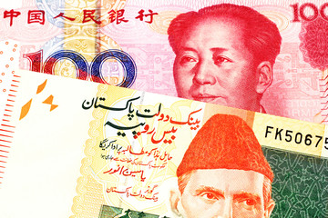 An orange and green twenty Pakistani rupee bank note with a red one hundred Chinese yuan bank note in macro