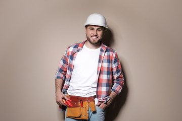 Young working man in hardhat standing on color background