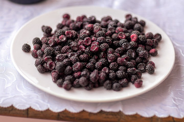 a plate of blackberries on a wooden table with a tablecloth,taken on a cloudy summer day