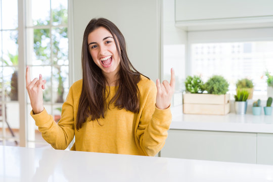 Beautiful young woman wearing yellow sweater shouting with crazy expression doing rock symbol with hands up. Music star. Heavy concept.