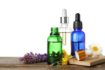 Bottles of different essential oils and wildflowers on wooden table, white background