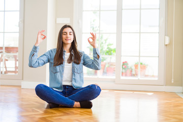 Fototapeta na wymiar Beautiful young woman sitting on the floor at home relax and smiling with eyes closed doing meditation gesture with fingers. Yoga concept.