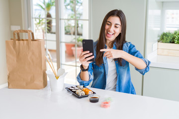 Beautiful young woman ordering food delivery from app using smartphone very happy pointing with hand and finger