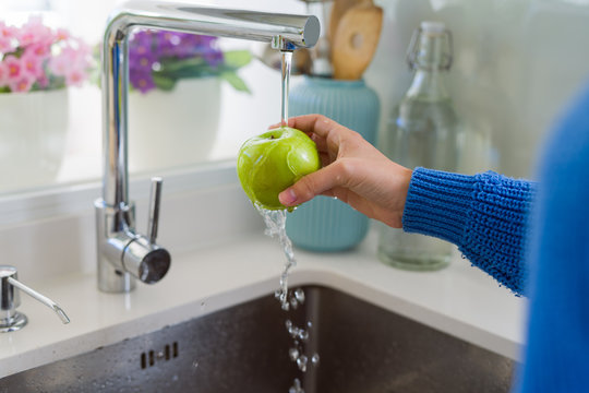 Young woman washing vegetables and fruit using water from sink