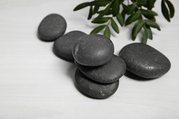 Spa stones with branch on light wooden background. Space for text