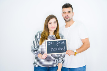 Young couple holding blackboard with our first home text over white isolated background with a...
