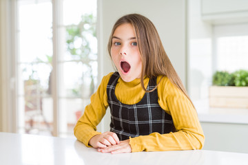 Young beautiful blonde kid girl wearing casual yellow sweater at home afraid and shocked with surprise and amazed expression, fear and excited face.