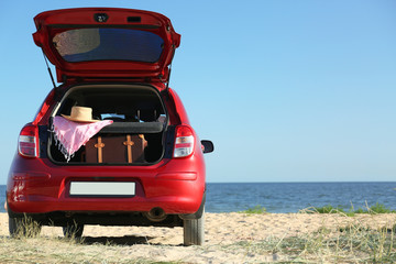 Retro suitcase and beach accessories in car trunk on sand near sea. Space for text