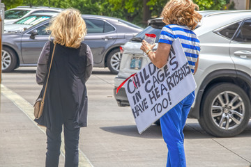 Protesting kids in cages - immigration issues -Two unidentifiable women protesters cross busy street - one carrying sign that says children have heartbeats too - obrazy, fototapety, plakaty