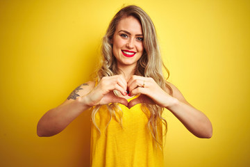 Young beautiful woman wearing t-shirt standing over yellow isolated background smiling in love showing heart symbol and shape with hands. Romantic concept.