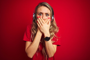 Young beautiful woman wearing headphones over red isolated background shocked covering mouth with hands for mistake. Secret concept.